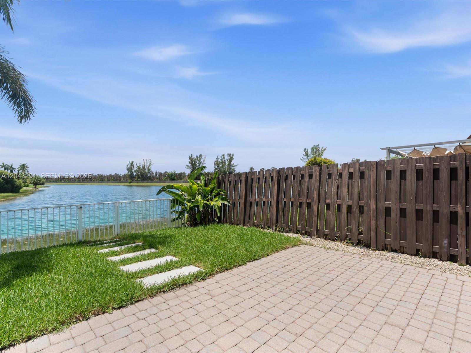 A backyard features a brick patio, a grassy lawn, a wooden fence, and a lake view — 11628 NW 87th Ln # 11628, Doral FL 33178, DORAL, FL