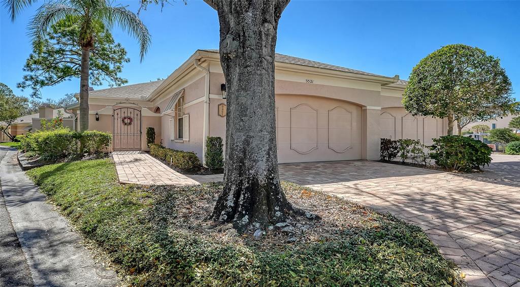 A single-story house with a paved driveway, a large tree, and a gated courtyard entrance — 5521 CHANTECLAIRE UNIT 21, SARASOTA, FL