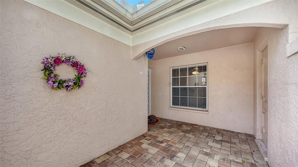 A covered entryway features a light-colored stucco wall, a floral wreath, and tiled flooring — 5521 CHANTECLAIRE UNIT 21, SARASOTA, FL