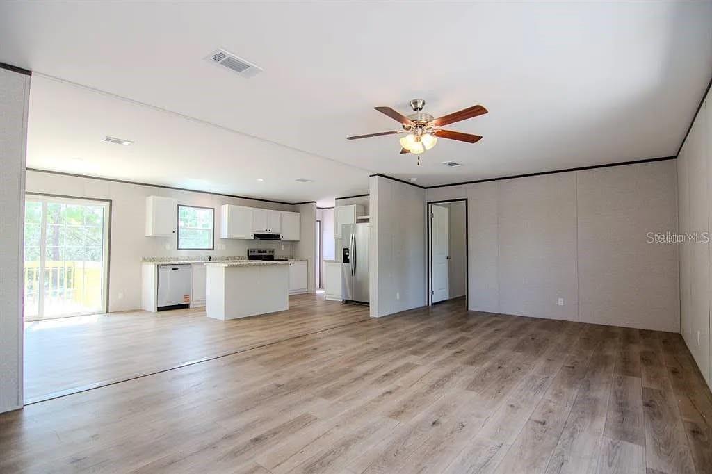 An open-concept living area features light wood-look flooring, a kitchen with white cabinets, and a ceiling fan — 16854 NW 254TH STREET, OKEECHOBEE, FL