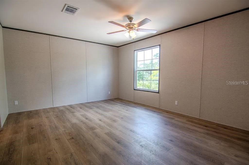 An empty bedroom features light-colored paneled walls, wood-look flooring, and a ceiling fan — 16854 NW 254TH STREET, OKEECHOBEE, FL