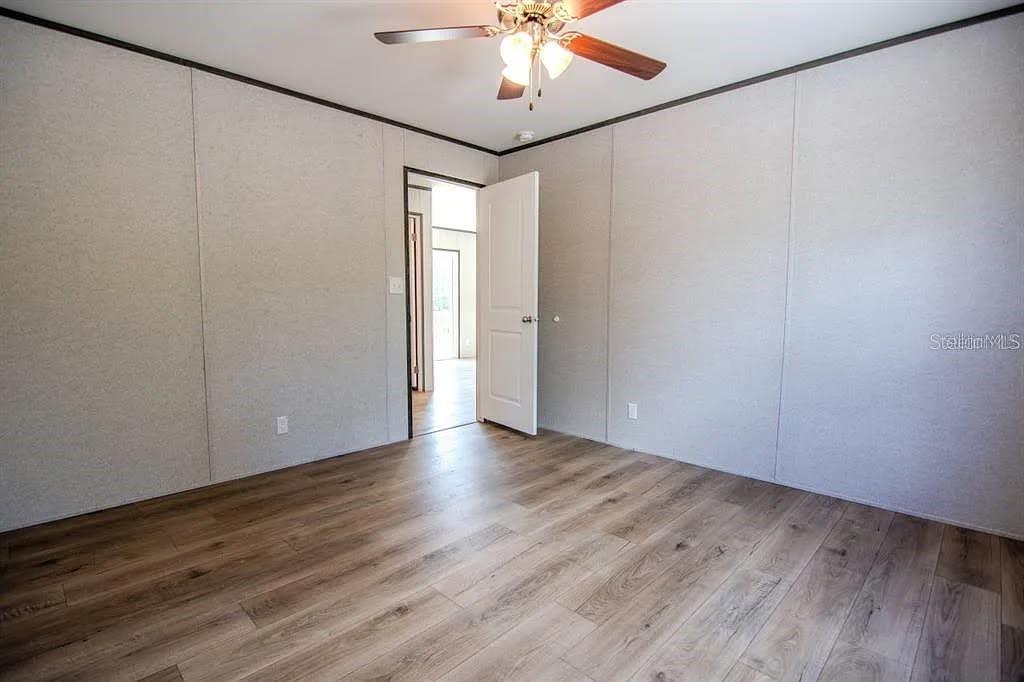 An empty room with light-colored paneled walls, wood-look flooring, and a ceiling fan — 16854 NW 254TH STREET, OKEECHOBEE, FL