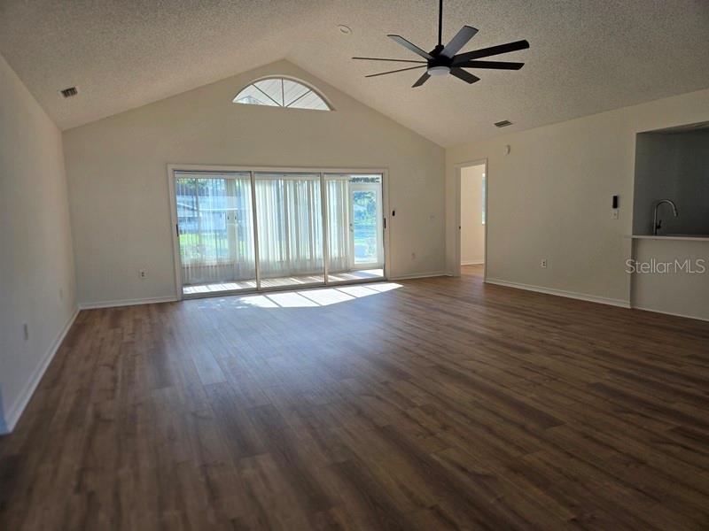 A spacious living room features vaulted ceilings, wood-look flooring, and sliding glass doors to a lanai — 11510 SW 85TH COURT, OCALA, FL