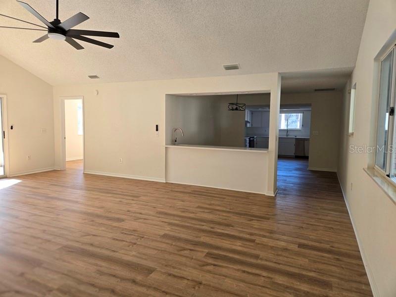 A living room with wood-look flooring, a ceiling fan, and a kitchen pass-through window — 11510 SW 85TH COURT, OCALA, FL