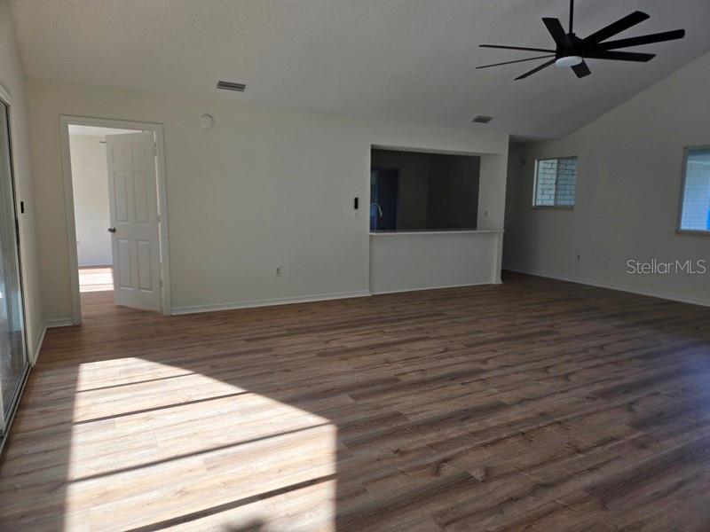 A spacious living room features wood-look flooring, a ceiling fan, and a kitchen pass-through window — 11510 SW 85TH COURT, OCALA, FL