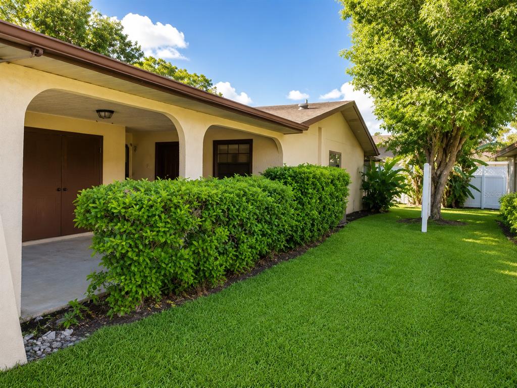 A house exterior features a covered porch, a manicured hedge, and a green lawn — 4808 HO WIL LANE, BRADENTON, FL
