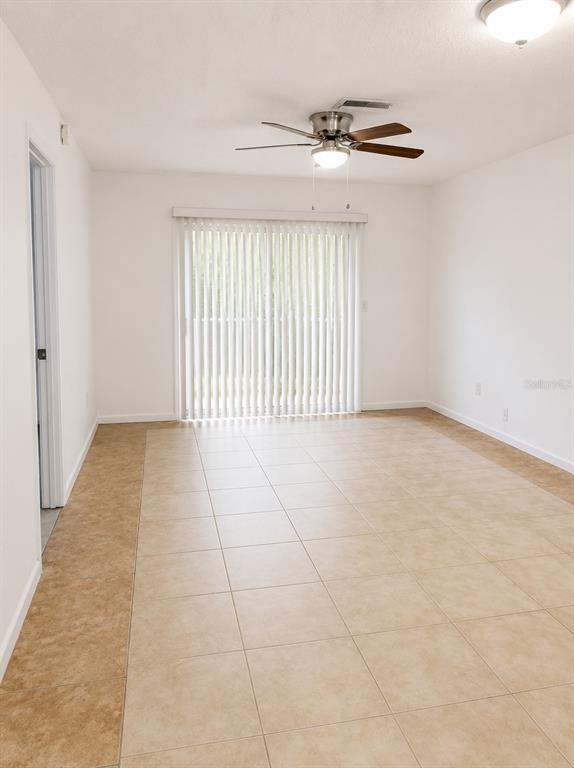 An empty room features light-colored tile flooring, a ceiling fan, and vertical window blinds — 4808 HO WIL LANE, BRADENTON, FL