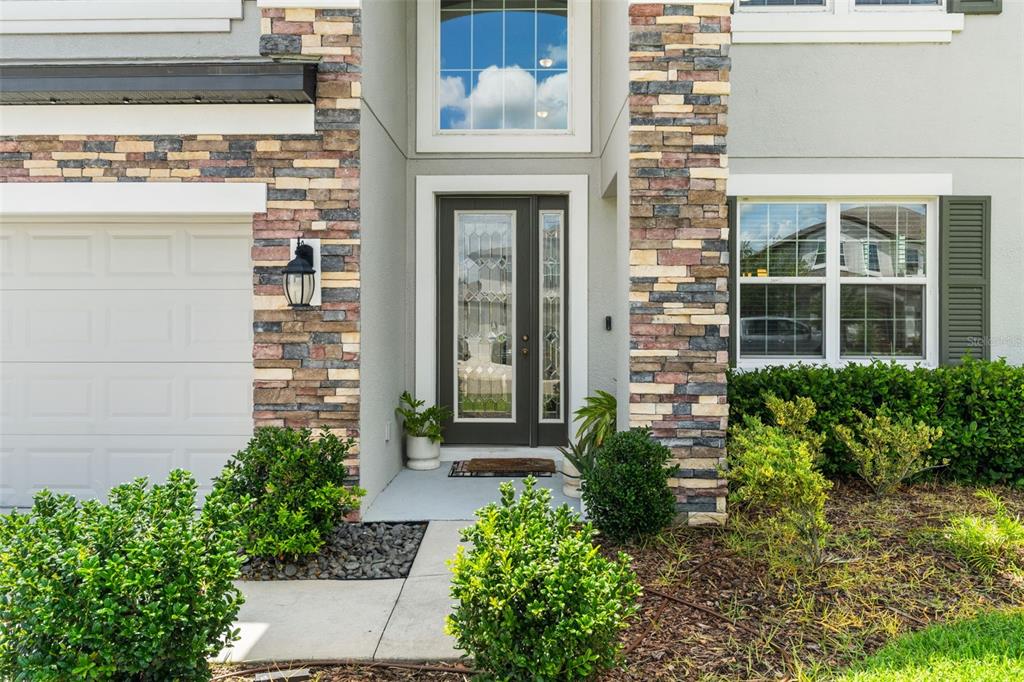 The exterior of a two-story home features a stone-accented facade, a dark front door, and landscaping — 7648 SWEETER TIDE TRAIL, WESLEY CHAPEL, FL