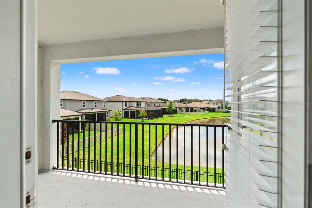 A covered balcony overlooks a grassy lawn, a pond, and neighboring houses — 7648 SWEETER TIDE TRAIL, WESLEY CHAPEL, FL
