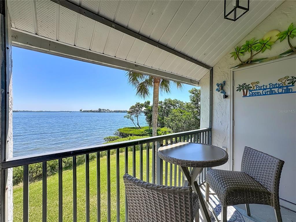 A covered balcony features a small table, two chairs, and a view of the water — 1801 GULF DRIVE N UNIT 293, BRADENTON BEACH, FL