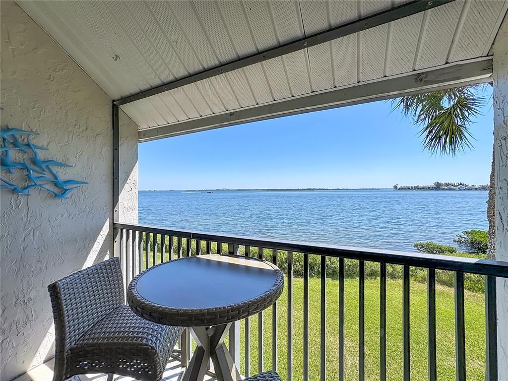 A covered balcony features a small table, a chair, and a view of the water — 1801 GULF DRIVE N UNIT 293, BRADENTON BEACH, FL