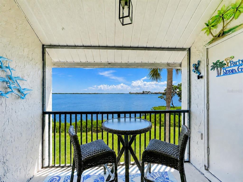 A covered balcony features a small round table, two chairs, and a view of water — 1801 GULF DRIVE N UNIT 293, BRADENTON BEACH, FL
