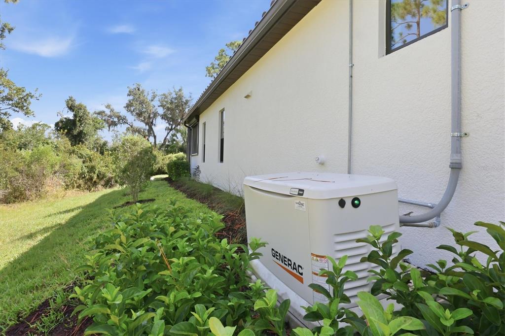 A Generac standby generator sits on the side of a house near landscaped bushes — 12946 TRUE BLUE CIRCLE, BRADENTON, FL