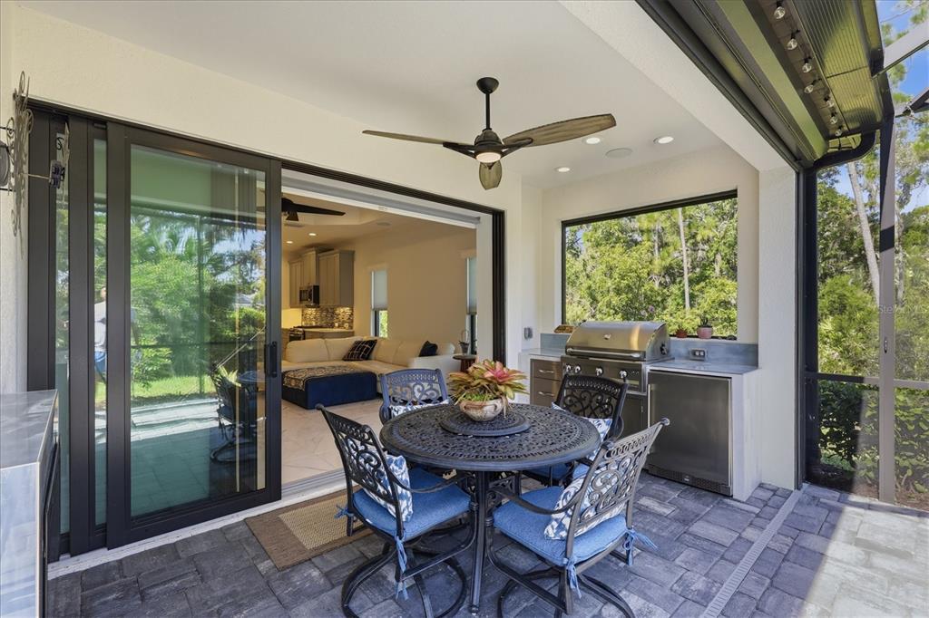 A covered patio features a dining set, an outdoor kitchen, and sliding doors to the interior — 12946 TRUE BLUE CIRCLE, BRADENTON, FL