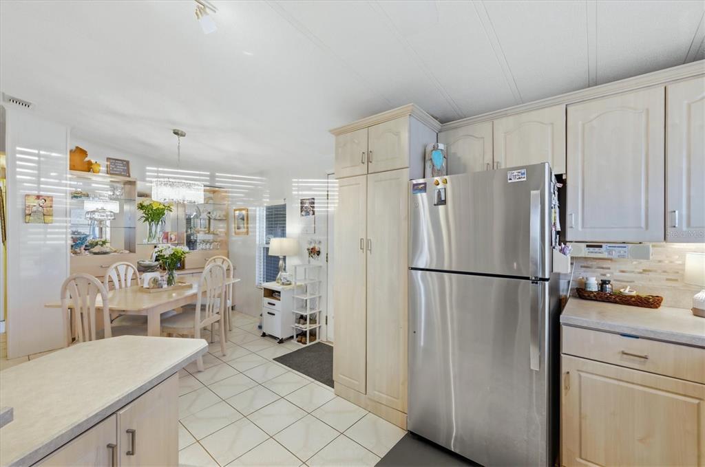 A kitchen with light wood cabinets and stainless steel appliances opens to a dining area — 727 BUTTERFIELD CIRCLE, ENGLEWOOD, FL