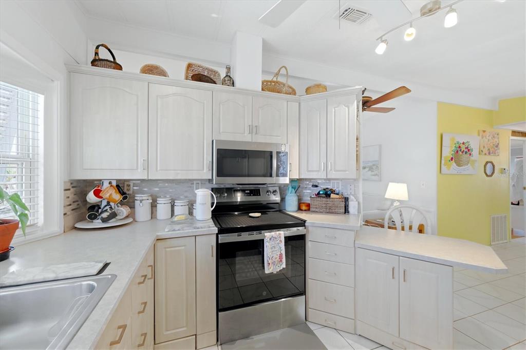 A kitchen features white cabinets, stainless steel appliances, and a yellow accent wall — 727 BUTTERFIELD CIRCLE, ENGLEWOOD, FL