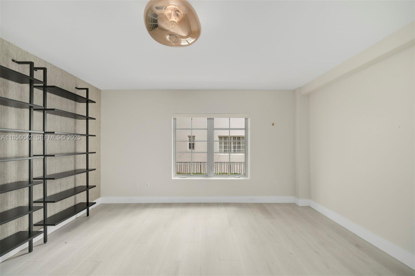 An empty room features light wood flooring, a black wall-mounted shelving unit, and a window — 435 21st St # 103, Miami Beach FL 33139, MIAMI BEACH, FL