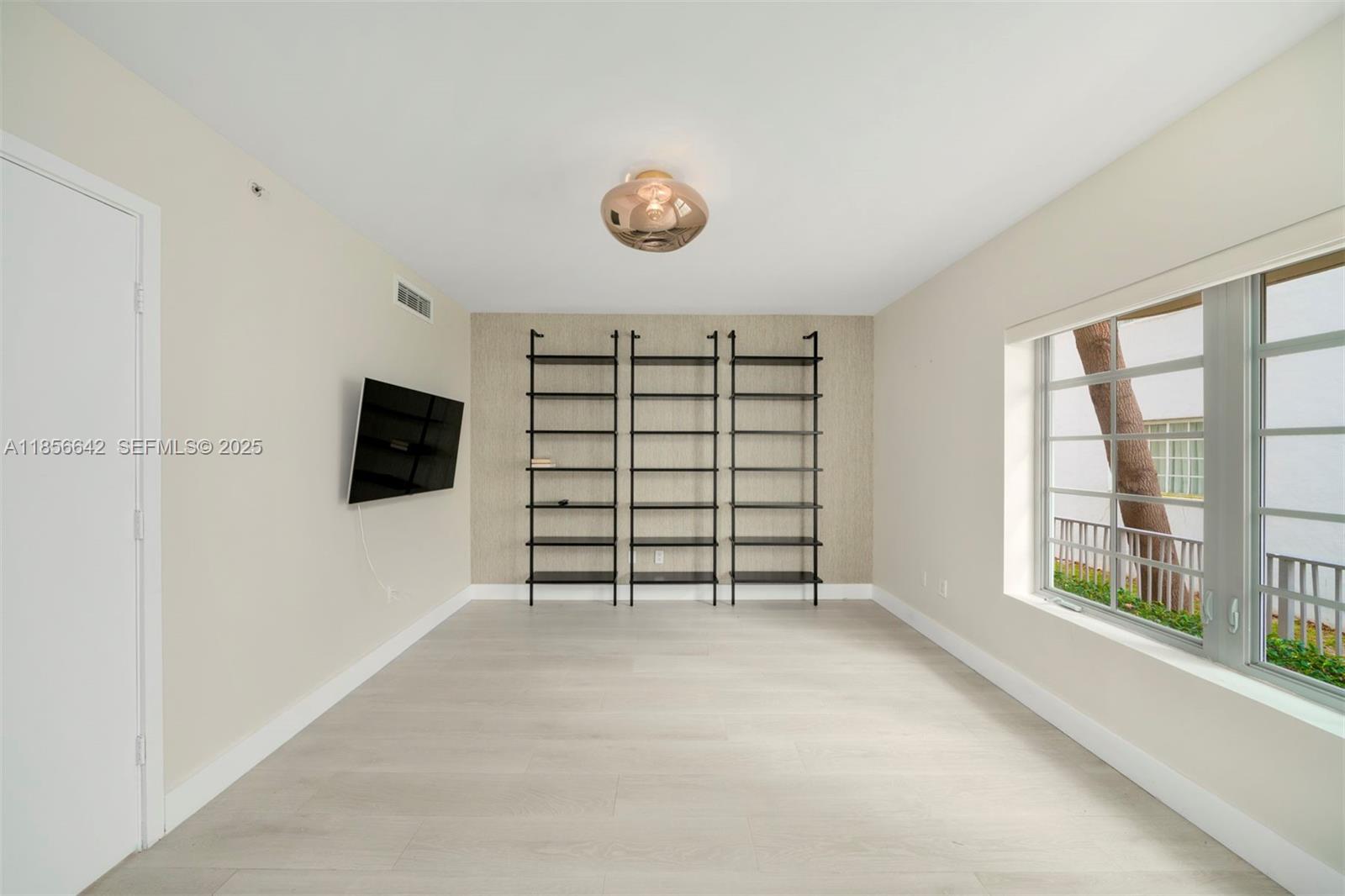 A room with light wood floors, three black metal shelves, and a wall-mounted television — 435 21st St # 103, Miami Beach FL 33139, MIAMI BEACH, FL