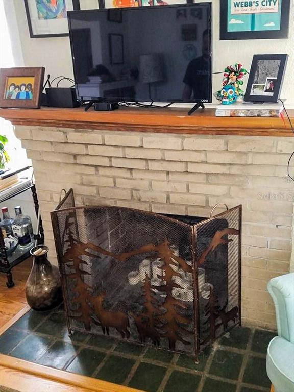 A brick fireplace features a decorative metal screen and a television on the wooden mantel — 1210 HIGHLAND STREET S, ST PETERSBURG, FL