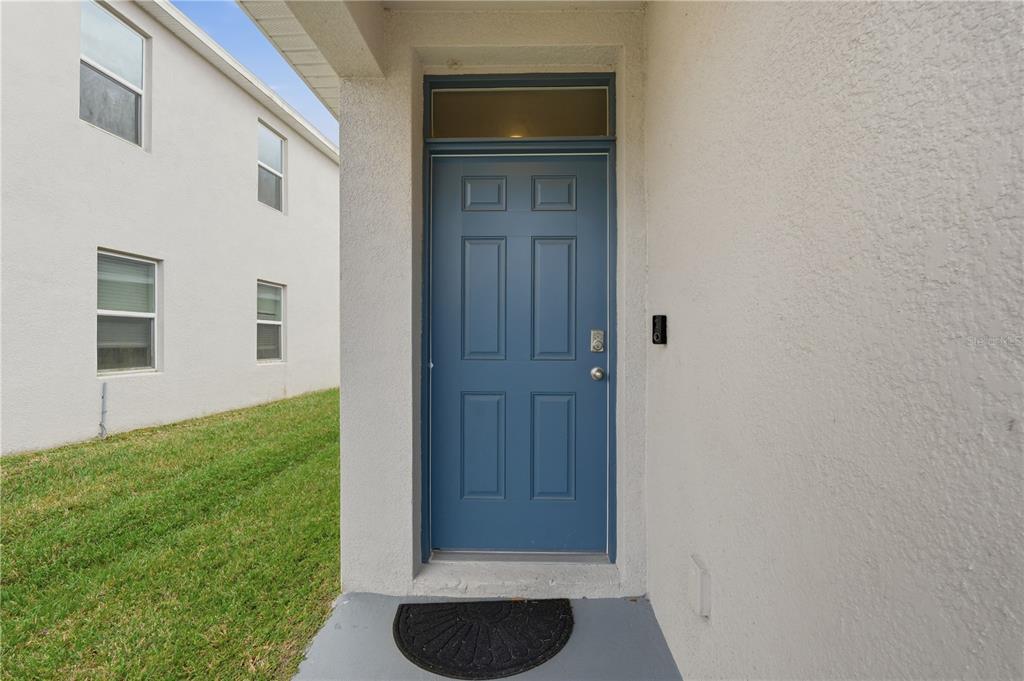 A blue front door with a transom window is set into a beige stucco exterior — 33922 JASPER STONE DRIVE, WESLEY CHAPEL, FL