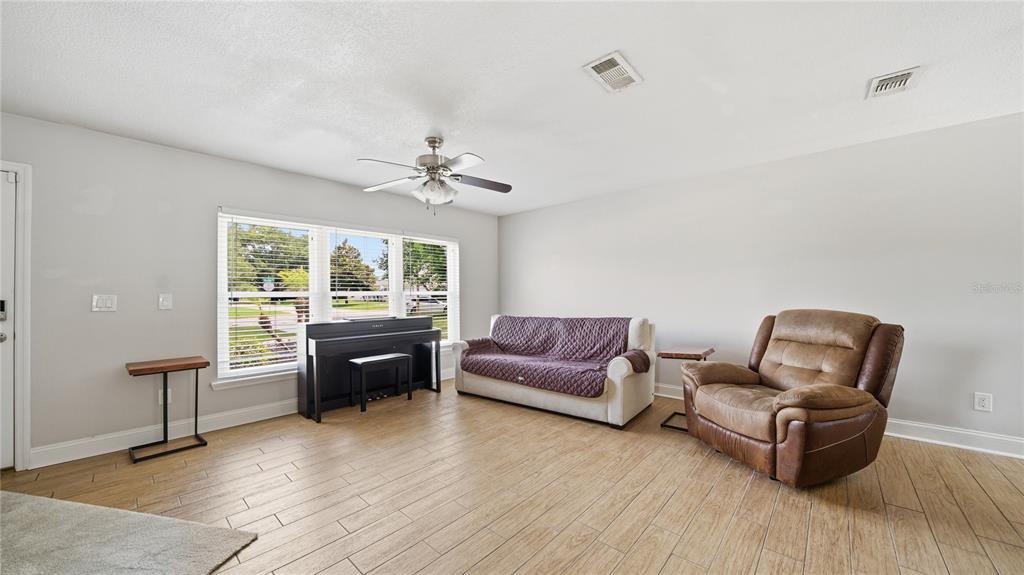 A living room features light wood-look tile flooring, a ceiling fan, a piano, and furniture — 125 BLUEFISH AVENUE, PONTE VEDRA BEACH, FL