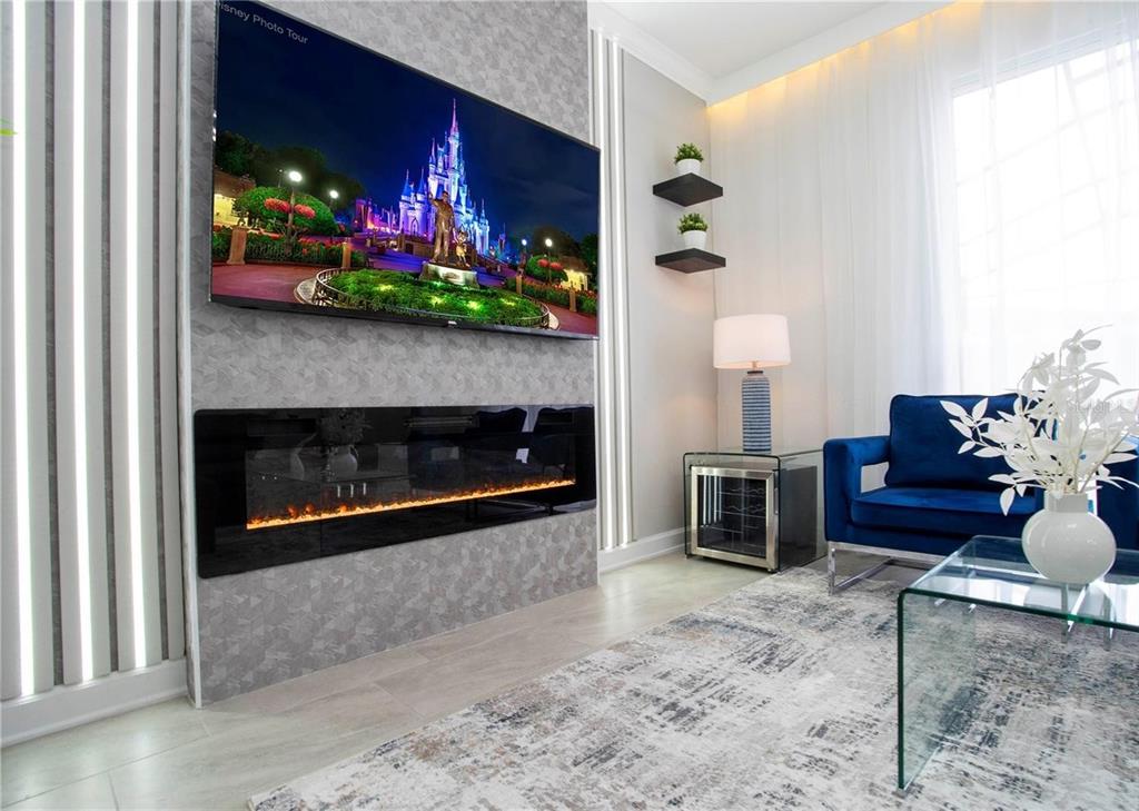 A living room features a wall-mounted television above a linear electric fireplace with textured tiling — 4289 PARAGRAPH DRIVE, KISSIMMEE, FL