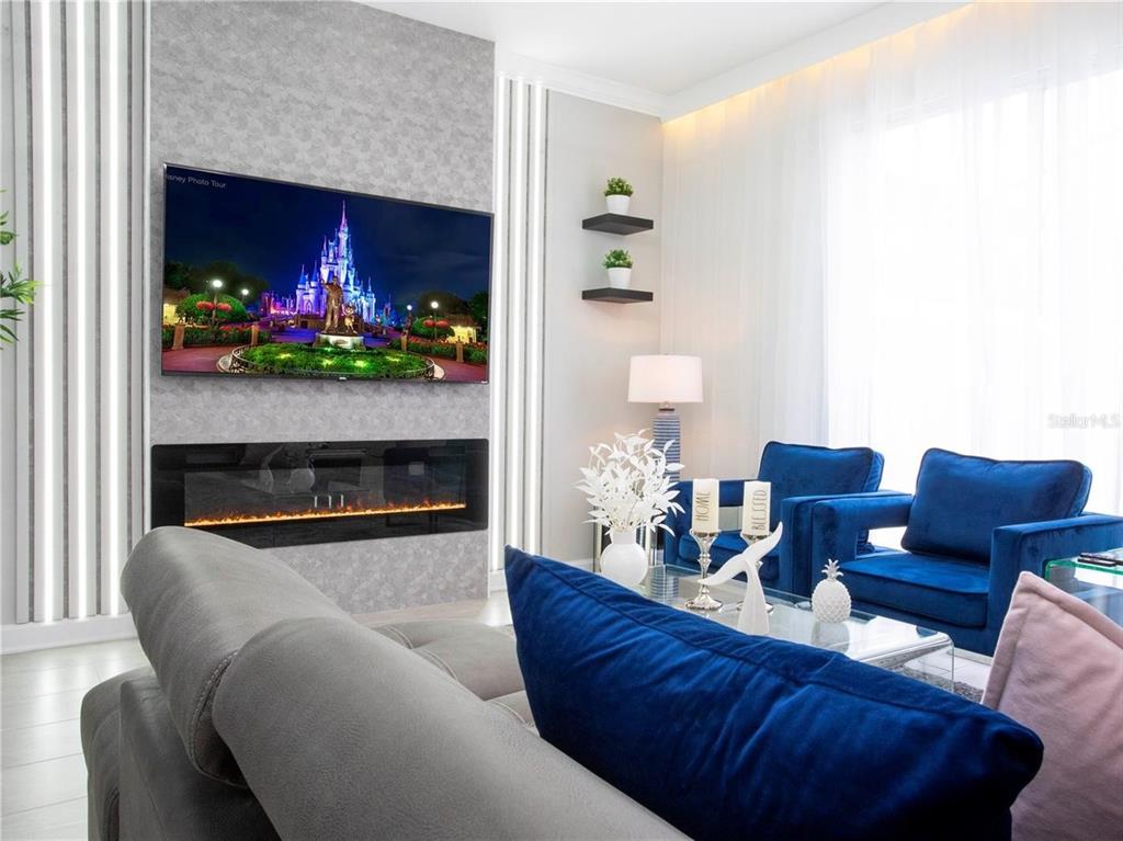 A living room features a wall-mounted television above a linear fireplace and blue velvet chairs — 4289 PARAGRAPH DRIVE, KISSIMMEE, FL