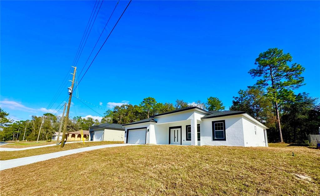 A white, single-story house with a garage and black window frames sits on a grassy lot — 10375 N CITRUS SPRINGS BOULEVARD, CITRUS SPRINGS, FL