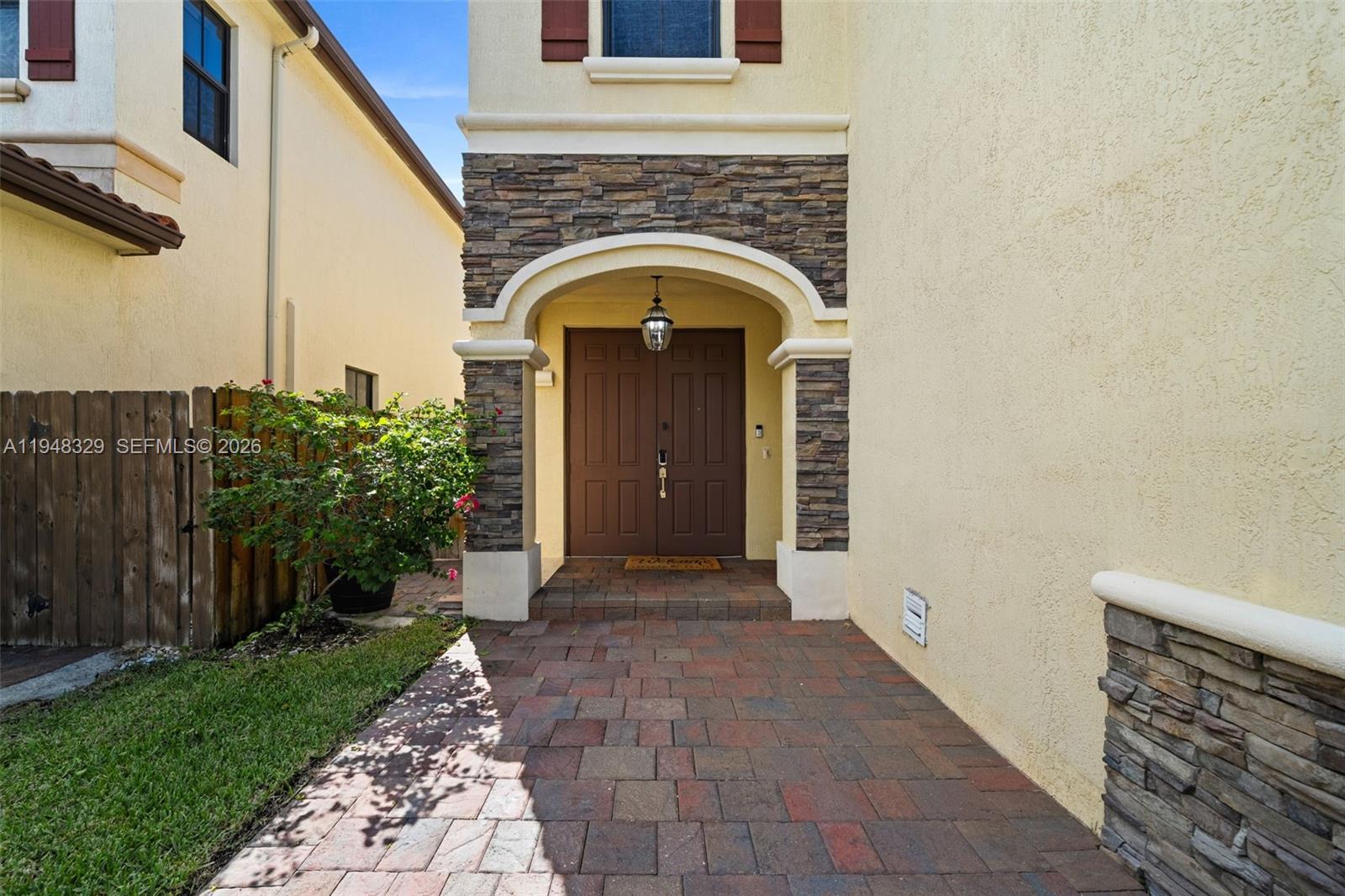 A paved walkway leads to a double-door entrance framed by stone veneer and an archway — 8658 NW 99th Path, Doral FL 33178, DORAL, FL