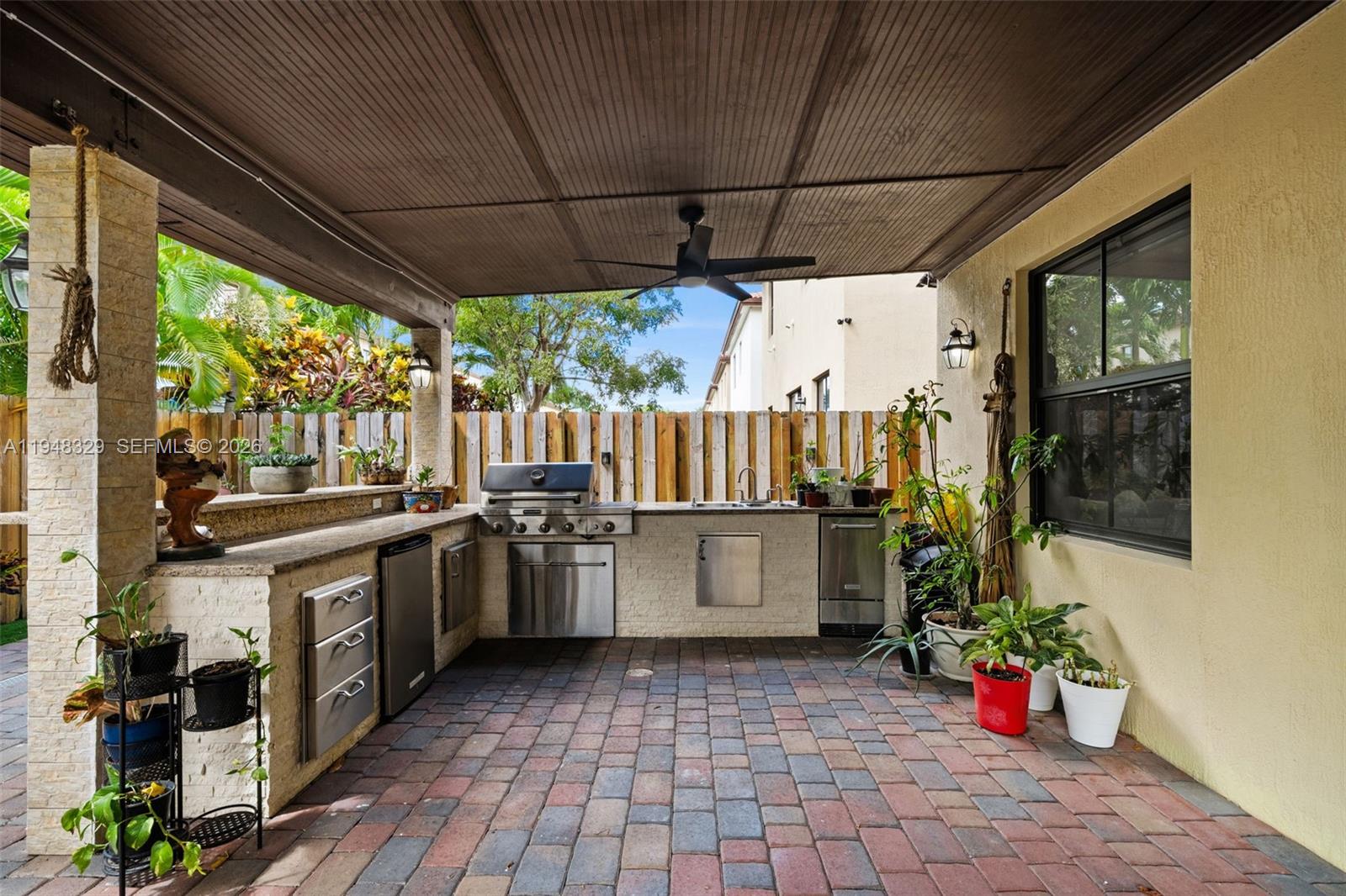 An outdoor kitchen features a stainless steel grill, sink, and stone counters under a patio — 8658 NW 99th Path, Doral FL 33178, DORAL, FL