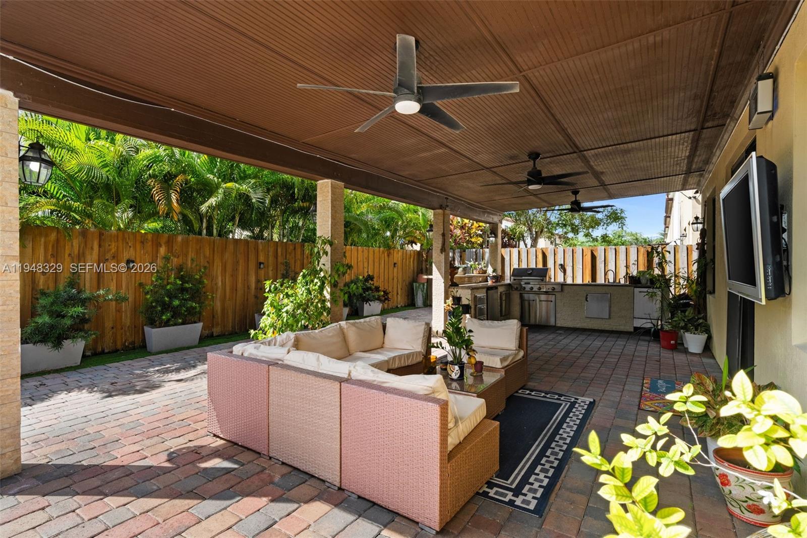 A covered outdoor patio features a brick floor, sectional seating, and a built-in kitchen area — 8658 NW 99th Path, Doral FL 33178, DORAL, FL