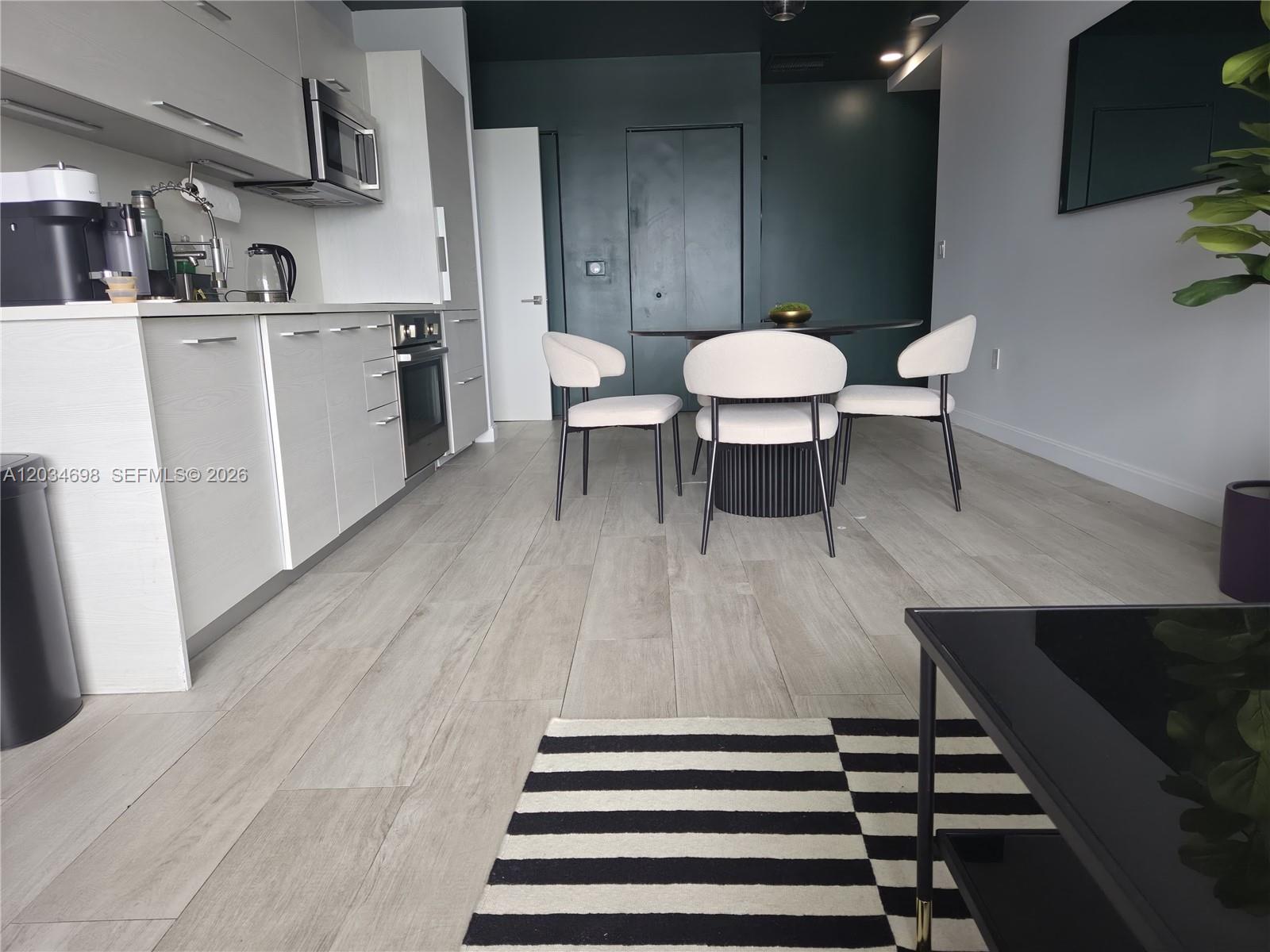 A modern kitchen and dining area feature light wood floors, white cabinetry, and dark accents — 45 SW 9th St # 4309, Miami FL 33130, MIAMI, FL