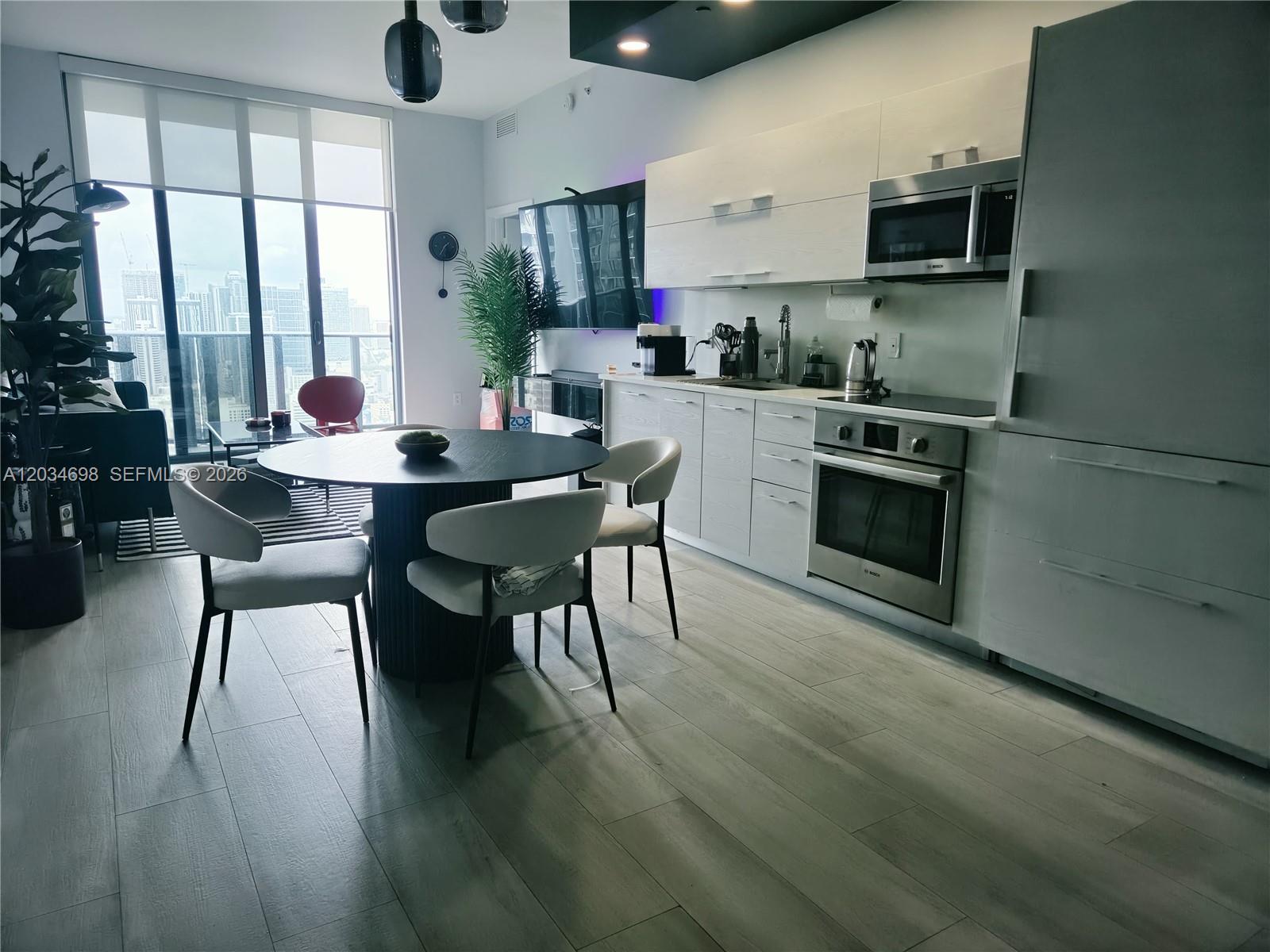 A modern kitchen and dining area feature light wood cabinetry, stainless steel appliances, and city views — 45 SW 9th St # 4309, Miami FL 33130, MIAMI, FL
