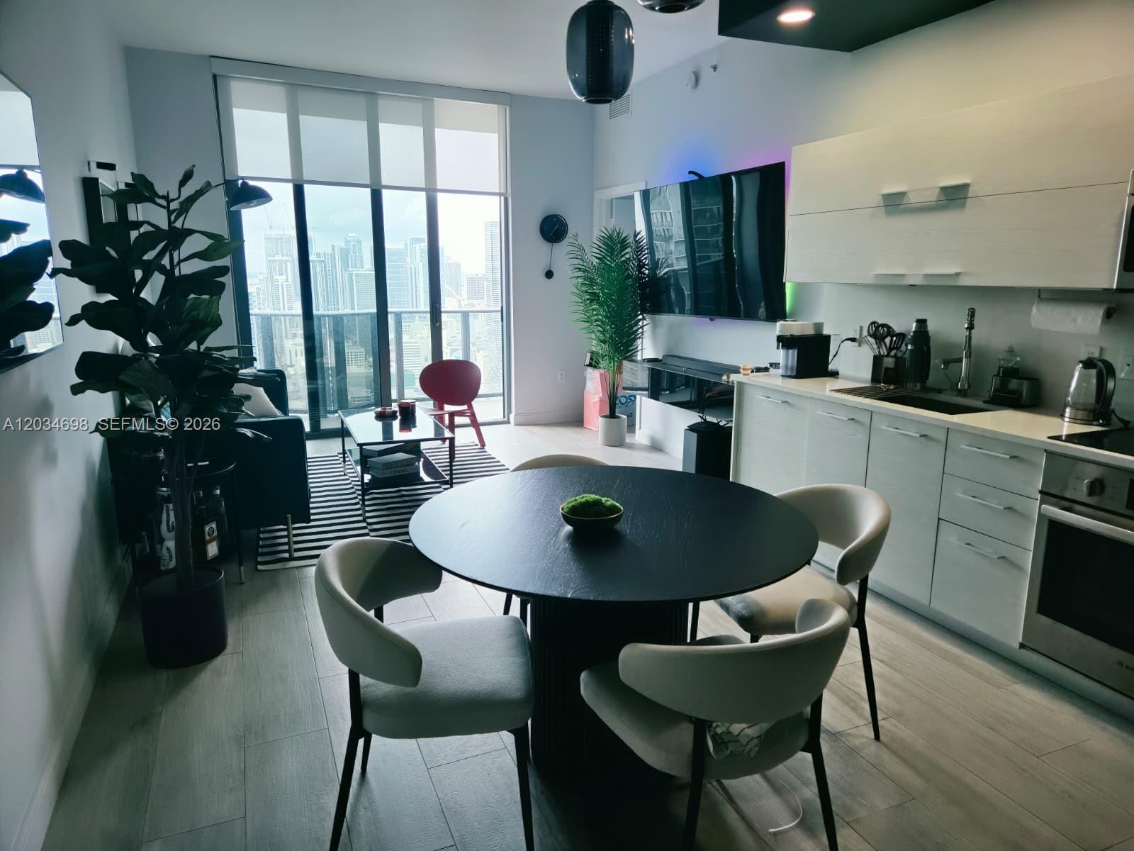 A modern apartment living and dining area features a round table, kitchen, and city views — 45 SW 9th St # 4309, Miami FL 33130, MIAMI, FL