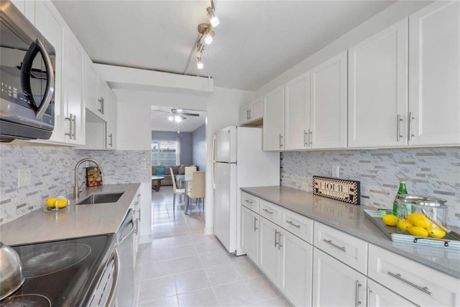 A galley kitchen features white cabinets, gray countertops, a tiled backsplash, and stainless steel appliances — 7500 NW 5th Court # 104, Margate FL 33063, MARGATE, FL