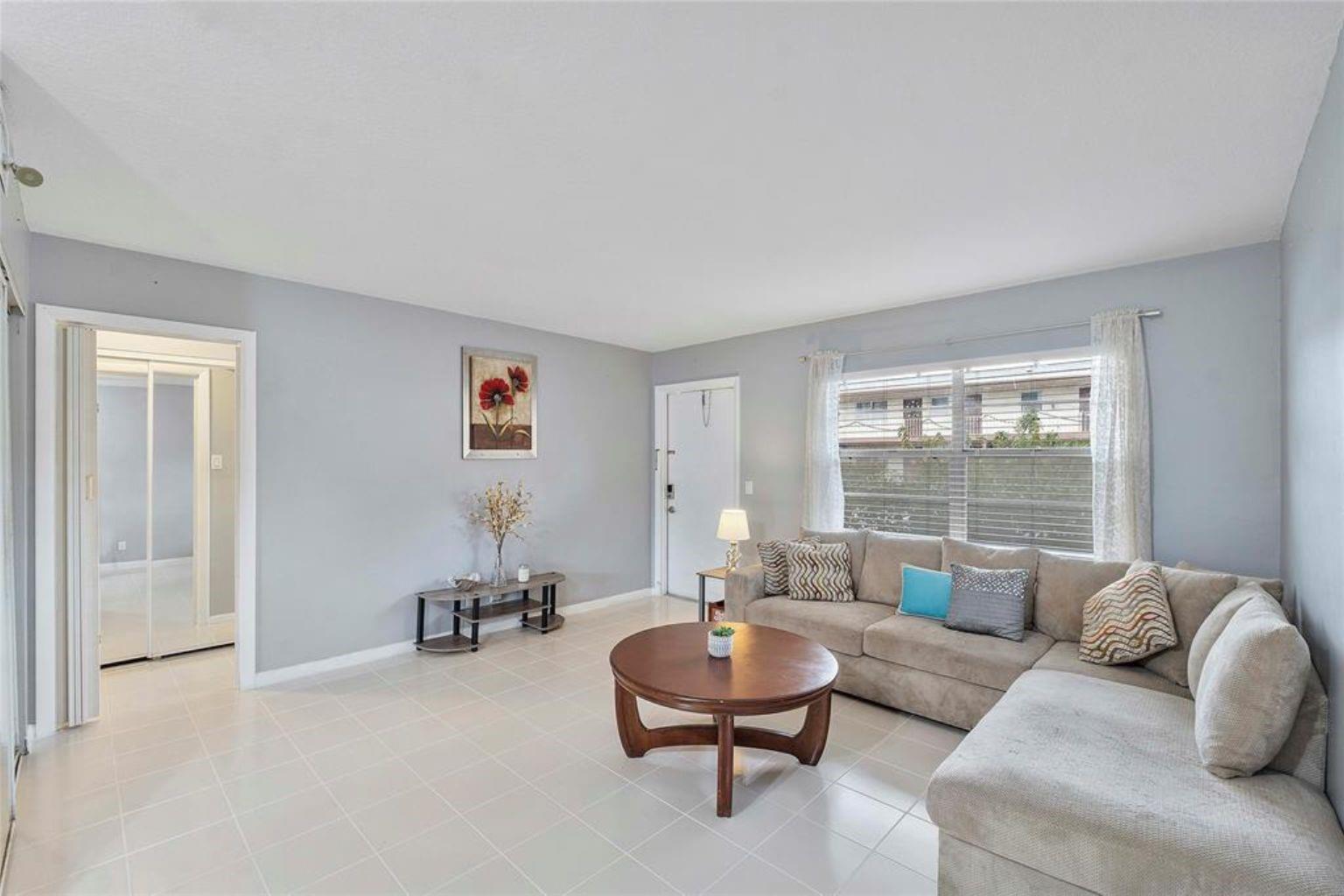 A living room features light gray walls, tile flooring, a beige sectional sofa, and windows — 7500 NW 5th Court # 104, Margate FL 33063, MARGATE, FL