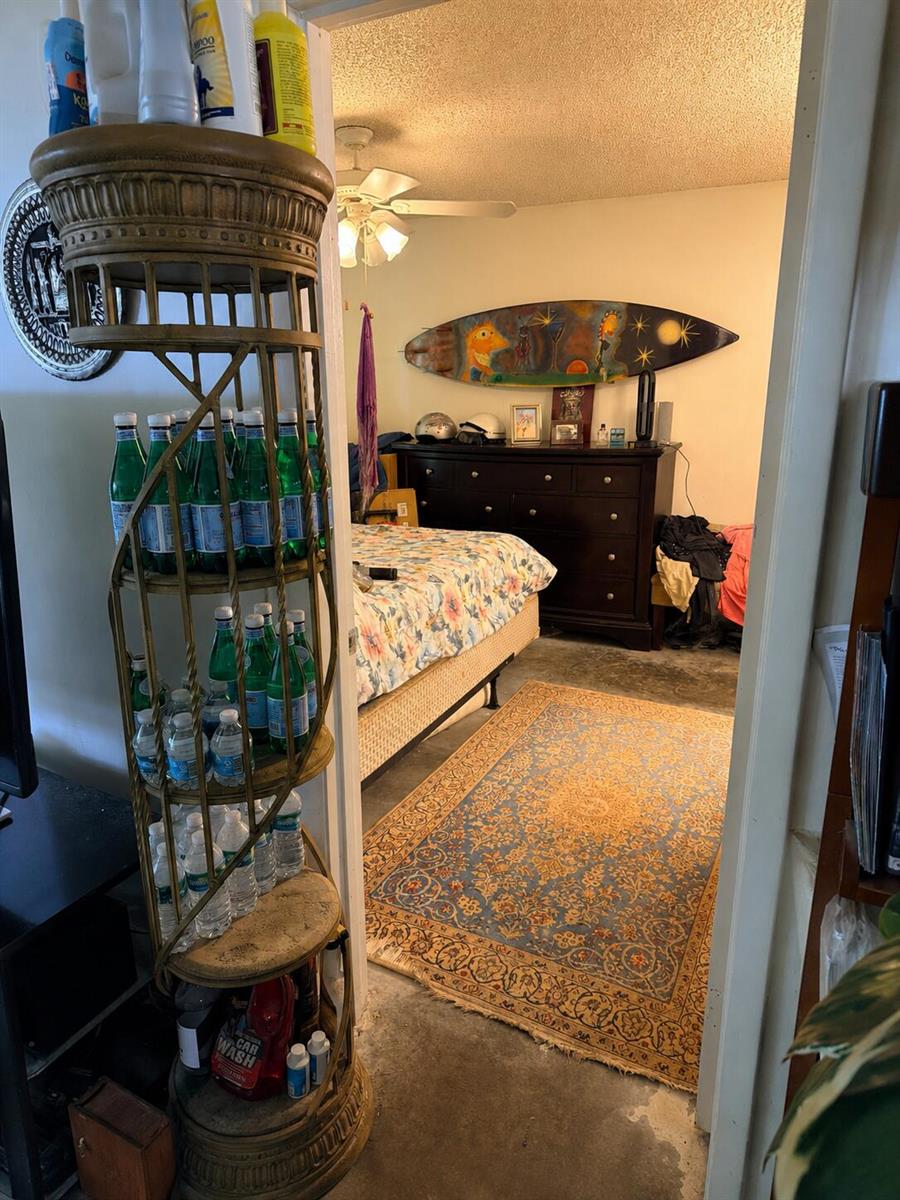 A bedroom with a floral bedspread, a dark dresser, and a decorative surfboard on the wall — 6323 La Costa Drive # B, Boca Raton FL 33433, BOCA RATON, FL