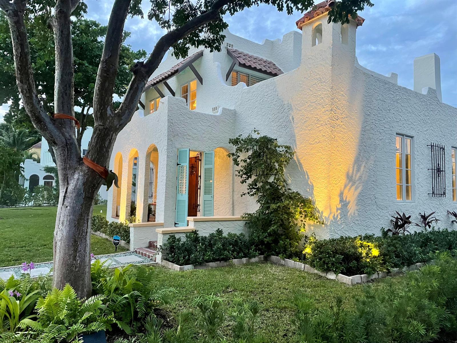 A white stucco house with arched entryways, turquoise shutters, and a tiled roof at dusk — 302 Fordham Drive, FL 33460, FL