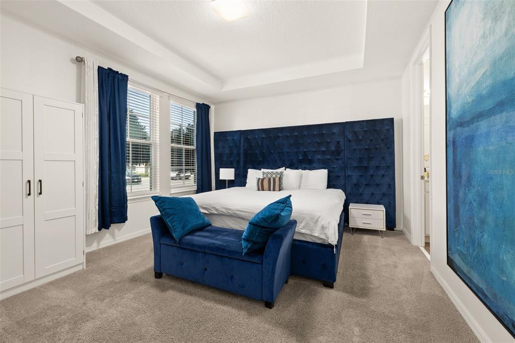 A bedroom features a tufted blue headboard, a matching bench, and a large abstract painting — 1539 CAREY PALM CIRCLE, KISSIMMEE, FL