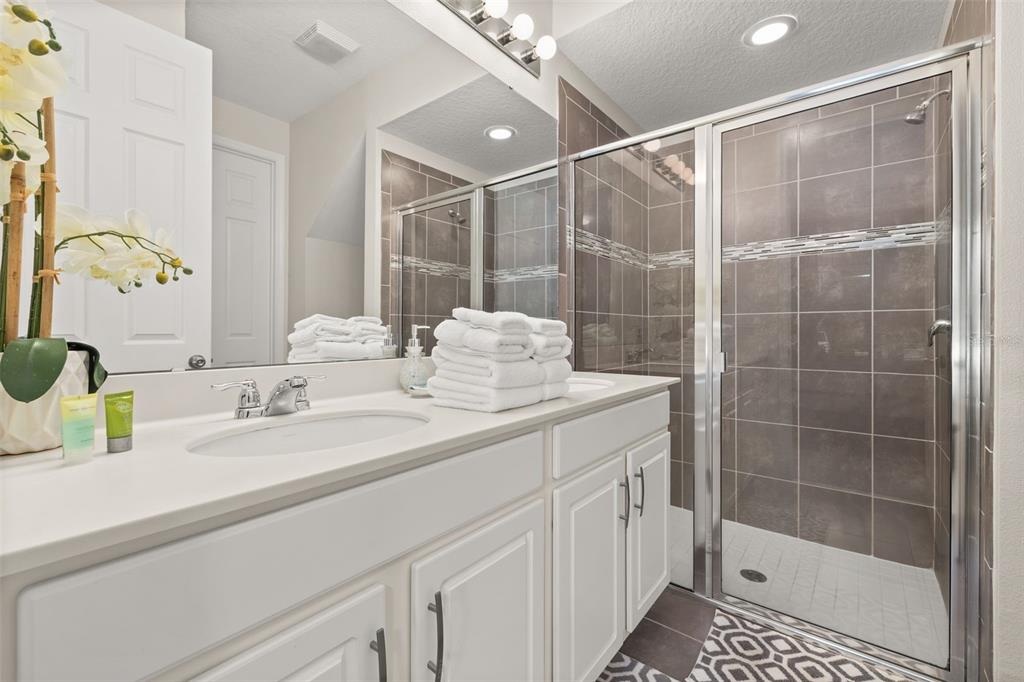 A bathroom features a white vanity with a double sink, a mirror, and a tiled shower — 1539 CAREY PALM CIRCLE, KISSIMMEE, FL