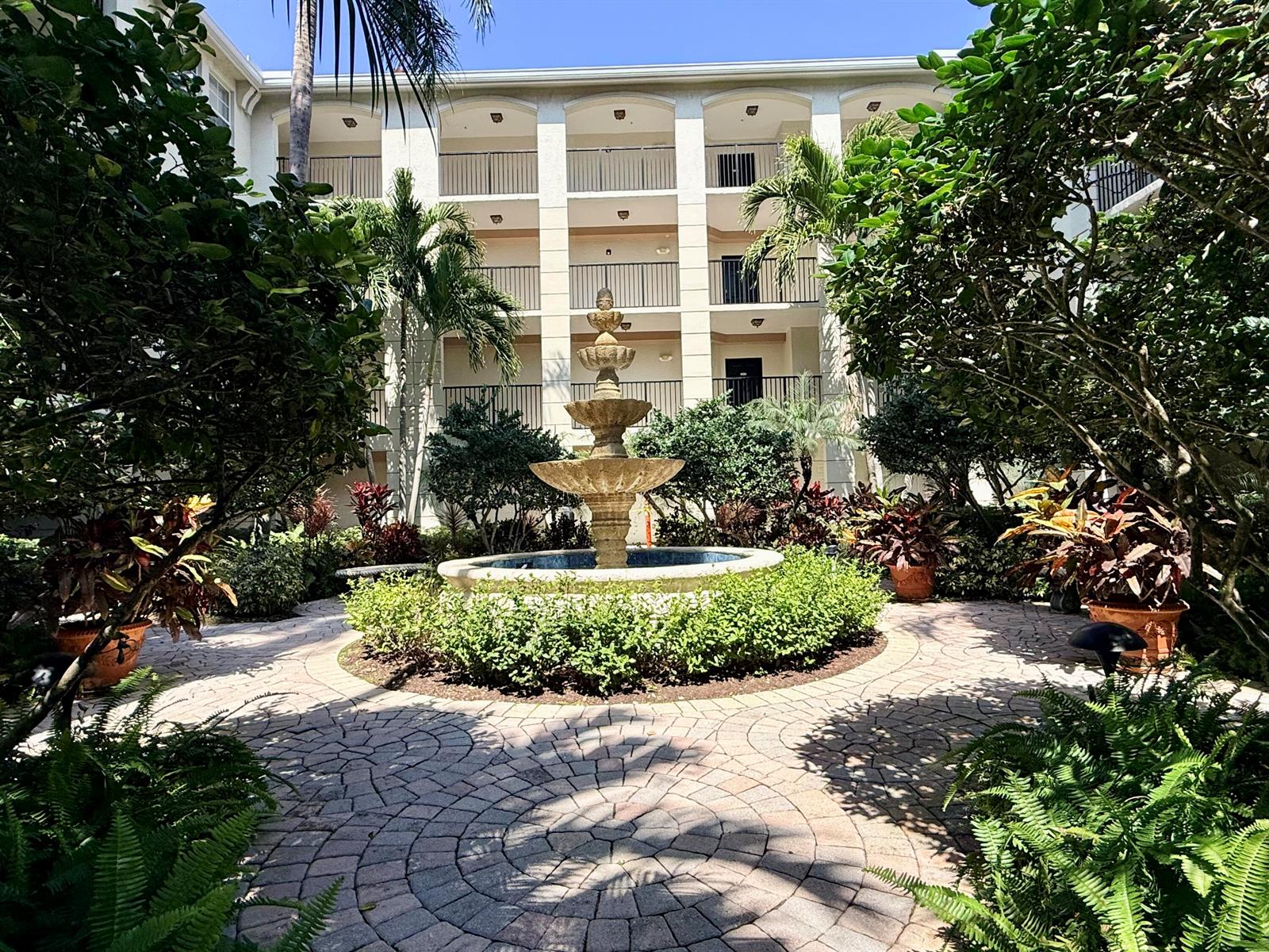 A tiered stone fountain sits in the center of a paved courtyard with lush landscaping — 4102 Tuscany Way # 4102, Boynton Beach FL 33435, BOYNTON BEACH, FL