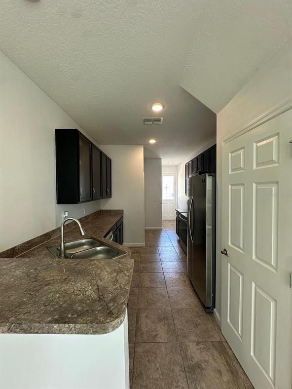A galley kitchen features dark cabinets, stainless steel appliances, and brown laminate countertops — 112 HOLLY VILLAGE DRIVE, DAVENPORT, FL