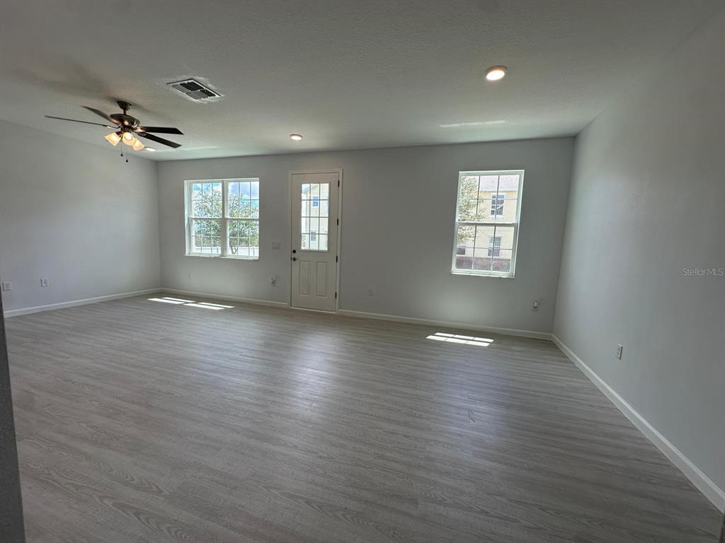 A spacious, unfurnished living room features light gray wood-look flooring, white walls, and a ceiling fan — 112 HOLLY VILLAGE DRIVE, DAVENPORT, FL