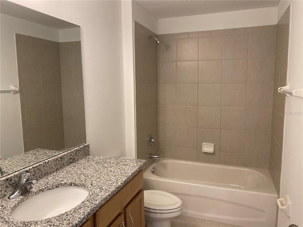 A bathroom features a granite vanity, a mirror, a toilet, and a tiled shower-tub combination — 10 PONTIAC LANE UNIT B, PALM COAST, FL
