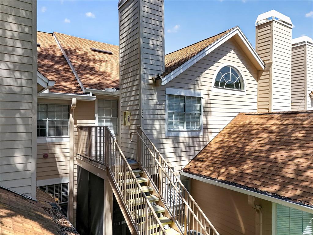 An exterior view shows a multi-story building with tan siding, a shingled roof, and stairs — 610 COLORADO PLACE UNIT 50, ALTAMONTE SPRINGS, FL