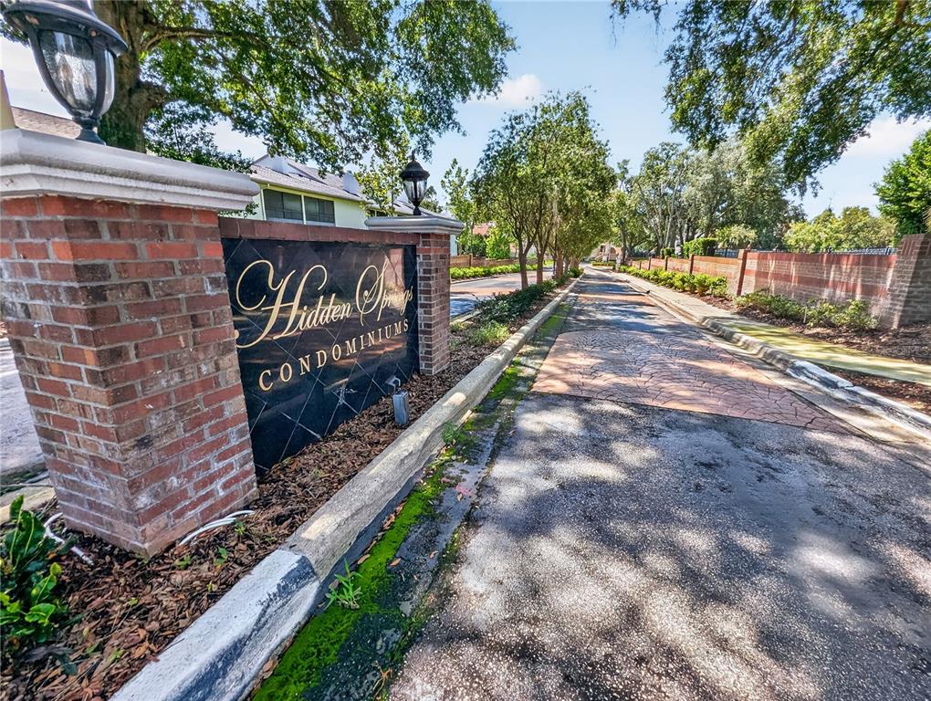 A brick entrance sign for Hidden Springs Condominiums stands beside a paved driveway — 610 COLORADO PLACE UNIT 50, ALTAMONTE SPRINGS, FL