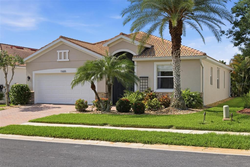 A single-story house with a tan stucco exterior, tile roof, and a two-car garage — 11655 ANHINGA AVENUE, VENICE, FL