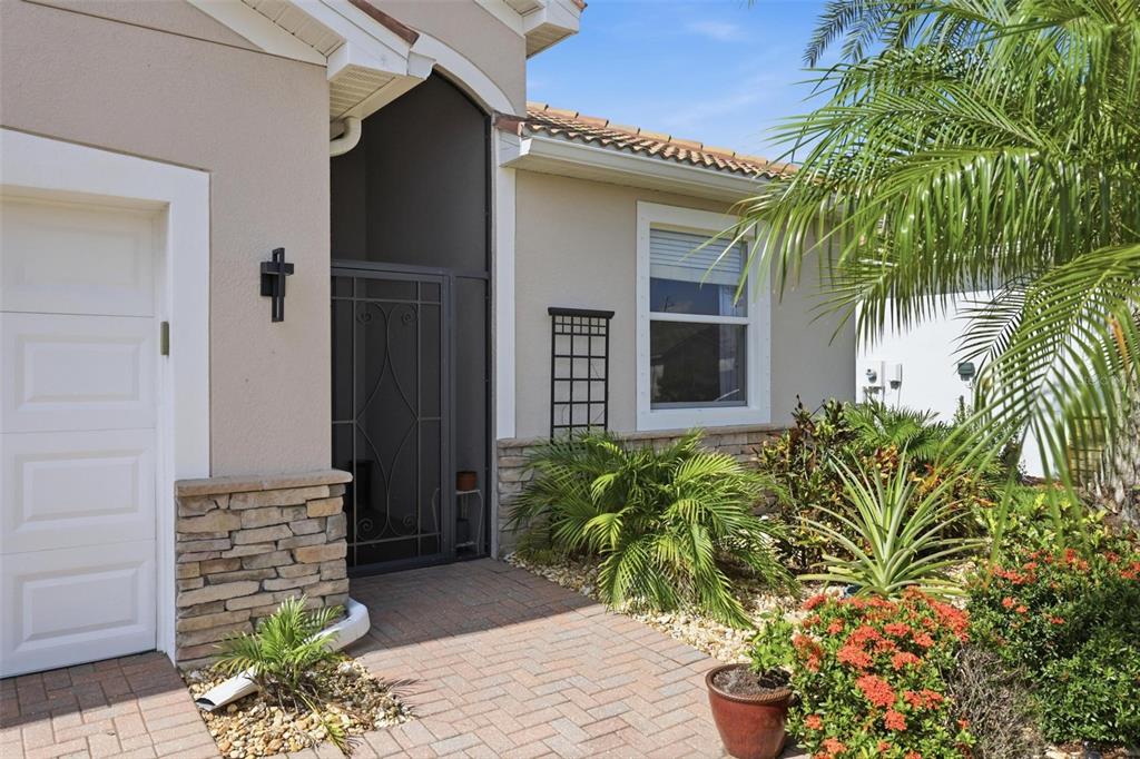 The exterior of a house features a brick walkway, stone accents, and a screen door — 11655 ANHINGA AVENUE, VENICE, FL