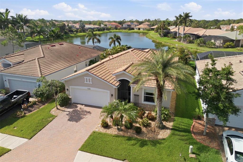 An aerial view shows a suburban house with a tile roof, driveway, and backyard lake — 11655 ANHINGA AVENUE, VENICE, FL