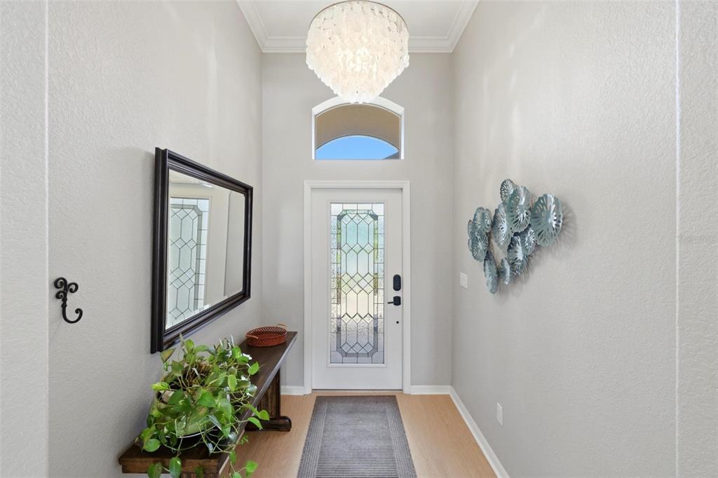 An entryway features a light wood floor, a console table, a mirror, and a chandelier — 11655 ANHINGA AVENUE, VENICE, FL